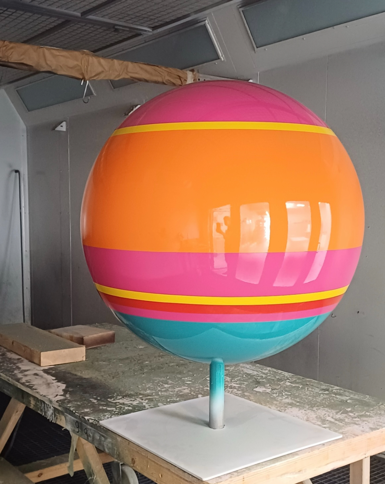 Sphere painted with glossy pink, orange, yellow and teal stripes in a spray booth
