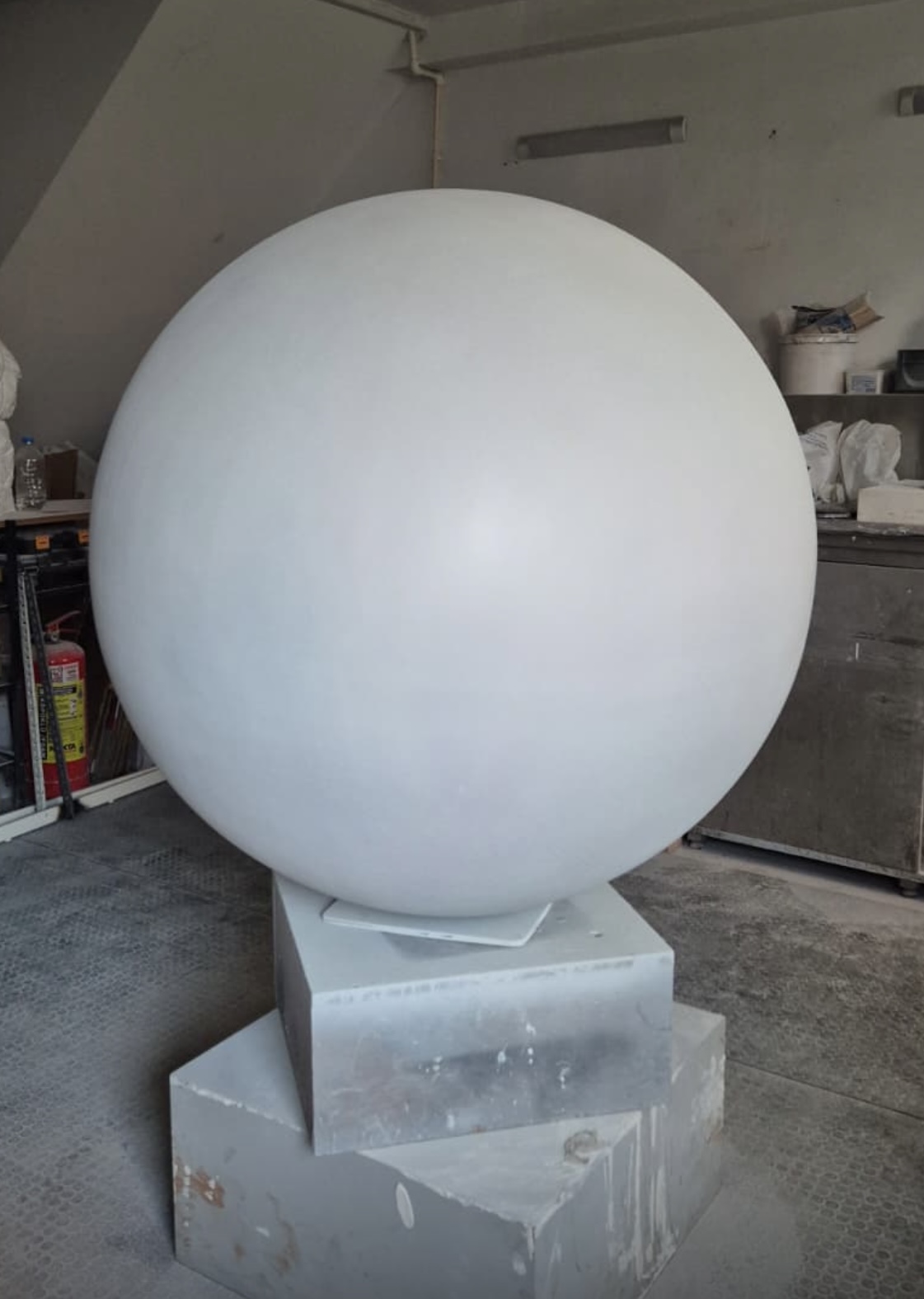 Large white primed sphere on a plinth in a fabrication workshop